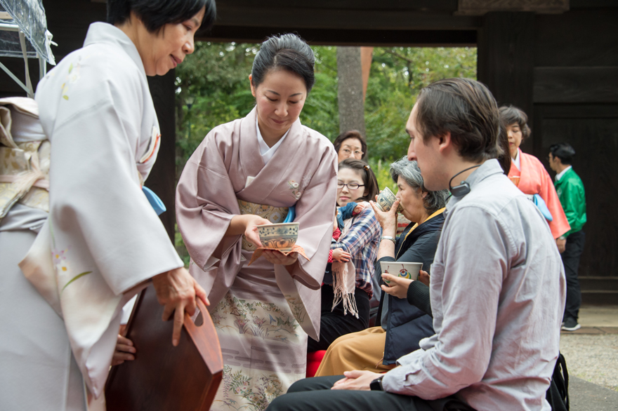 Photograph of event participant receiving a cup of green tea from a woman in a kimono