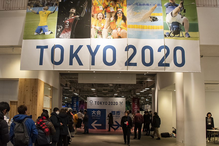 Volunteers line up at the venue entrance decorated with a Tokyo 2020 banner and athlete photographs